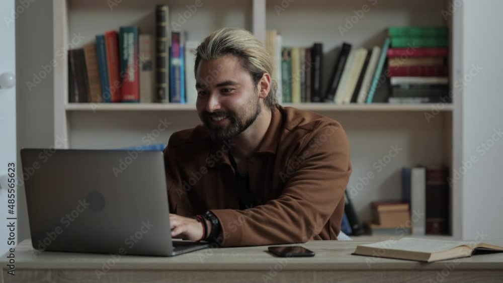 Excited caucasian man in casual wear pointing finger up while using laptop at home. Smartphone and book lying on table. Inspiration and idea concept. Excited caucasian man in casual wear pointing finger up while using laptop at home. Smartphone and book lying on table. Inspiration and idea concept.