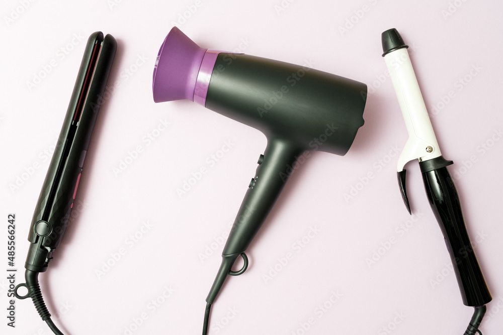 Fototapeta premium hair dryer, curling iron, straightener in black on purple background, professional hairdresser set