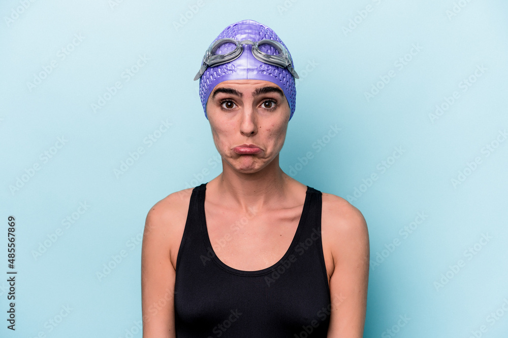 Young swimmer woman isolated on blue background shrugs shoulders and open eyes confused. Young swimmer woman isolated on blue background shrugs shoulders and open eyes confused.