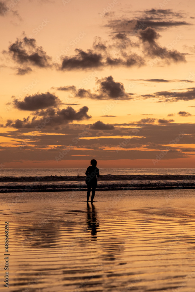 vertical portrait, Silhouette of a woman enjoying a sunset on a beach in Costa Rica.