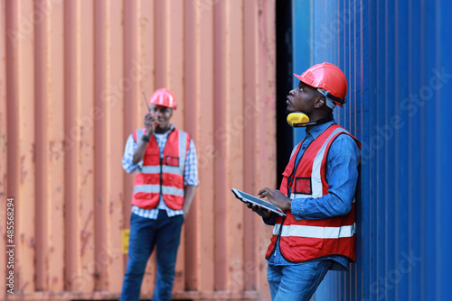 Foreman using tablet and walkie talkie radio control loading containers box. Engineer or worker with safety hat work at container cargo site and checking industrial container cargo freight ship.