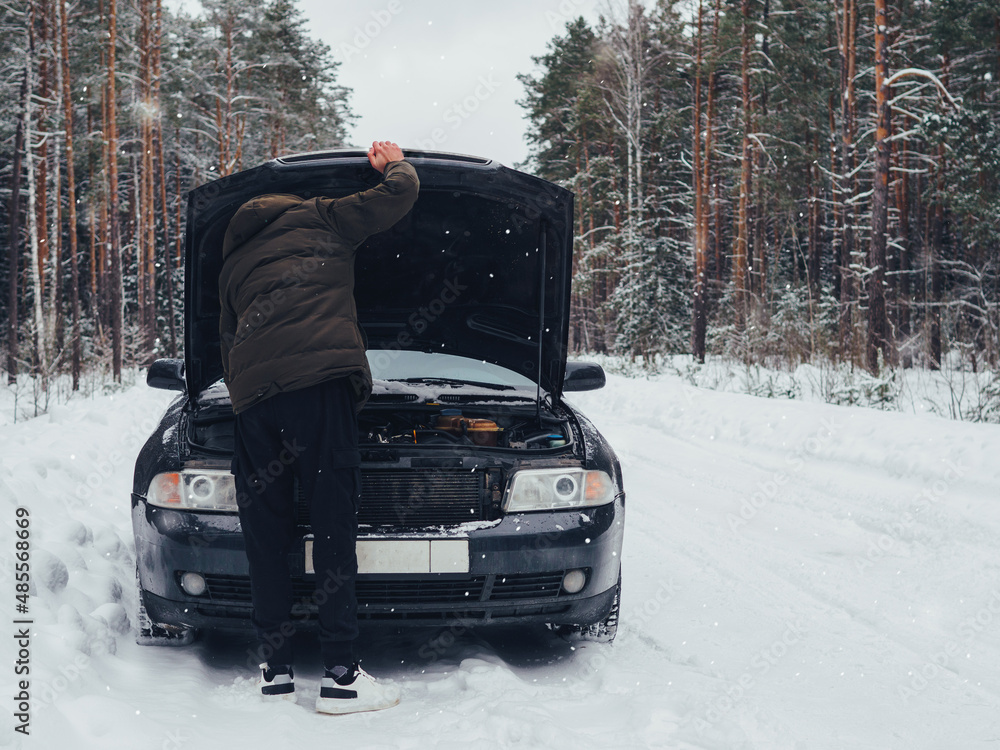The driver looks under the hood of his car. Breakdown on a winter snow-covered forest road. Repair the car