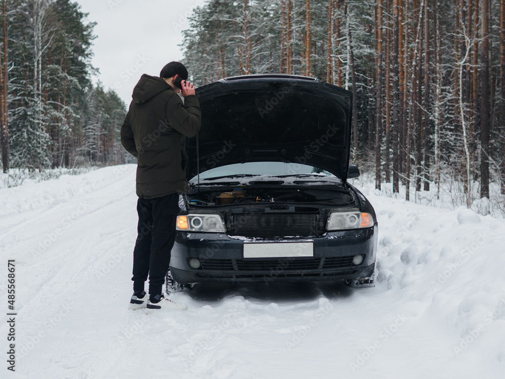 A car breakdown on a snowy winter road. Male driver uses phone to call tow truck or help