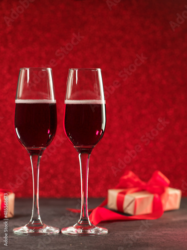 Two glasses of cider or champagne on a red side background and gift boxes