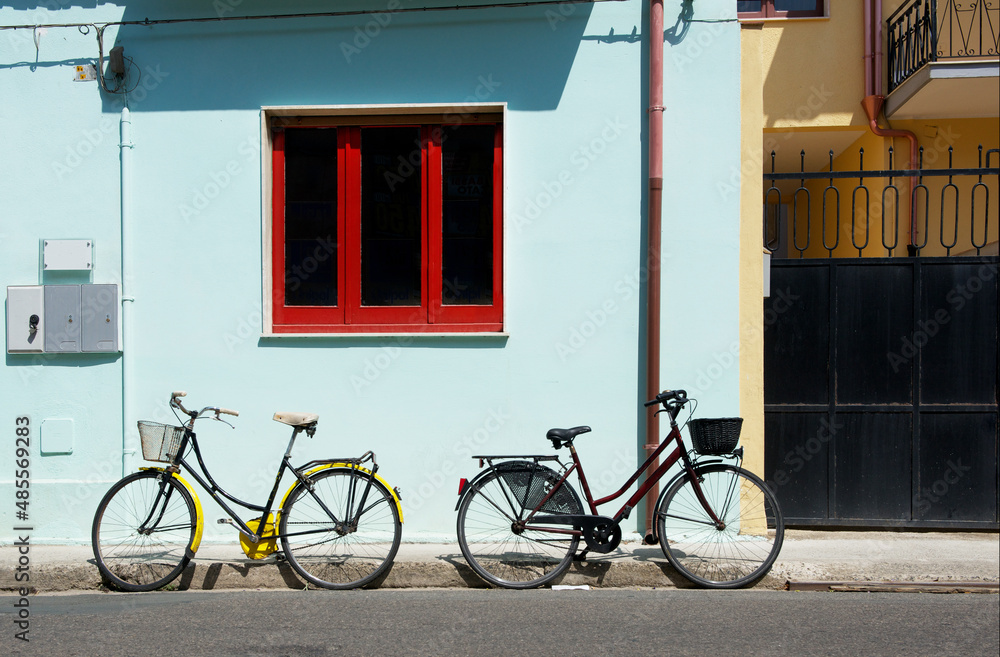 Active life style concept - two bicycles near house in sunny summer day. No people, horizontal photo. Two bicycles in the street, transport. Yellow and red bicycles in the street Active life style concept - two bicycles near house in sunny summer day. No people, horizontal photo. Two bicycles in the street, transport. Yellow and red bicycles in the street