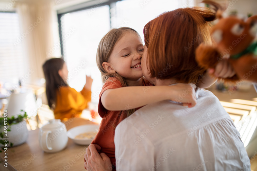 Rear view of mother hugging her little daughter in kitchen at home. Rear view of mother hugging her little daughter in kitchen at home.