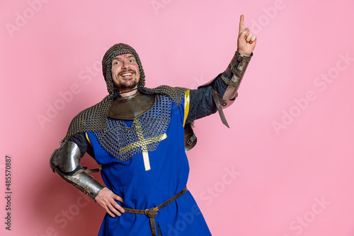 Porrait of excited man, medieval warrior or knight in protection rising finger expressing idea isolated over pink studio background