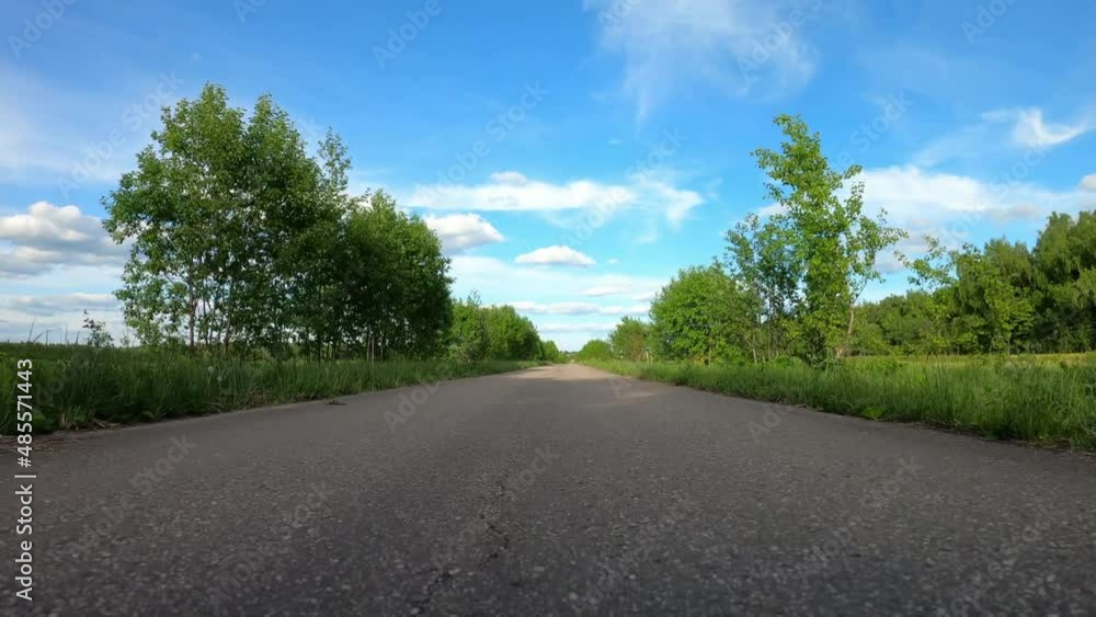 Tracking shot of road across a field. POV camera moving forward. Bumper view. Beautifull forest. cloudy sky. bright sun. Concept of endless road. Tracking shot of road across a field. POV camera moving forward. Bumper view. Beautifull forest. cloudy sky. bright sun. Concept of endless road.
