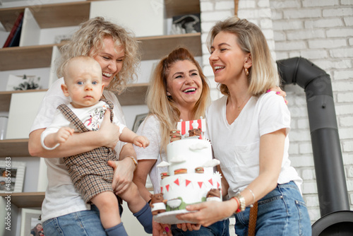 group of three attractive woman in gleaming room with baby. Women having fun with son, showing him huge birthday cakec