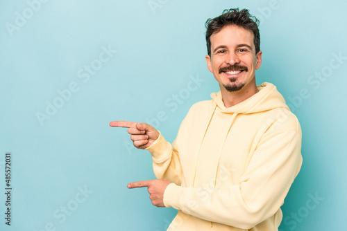 Young caucasian man isolated on blue background excited pointing with forefingers away.