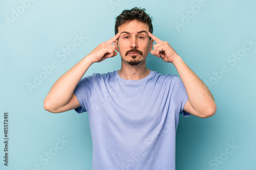 Young caucasian man isolated on blue background focused on a task, keeping forefingers pointing head.