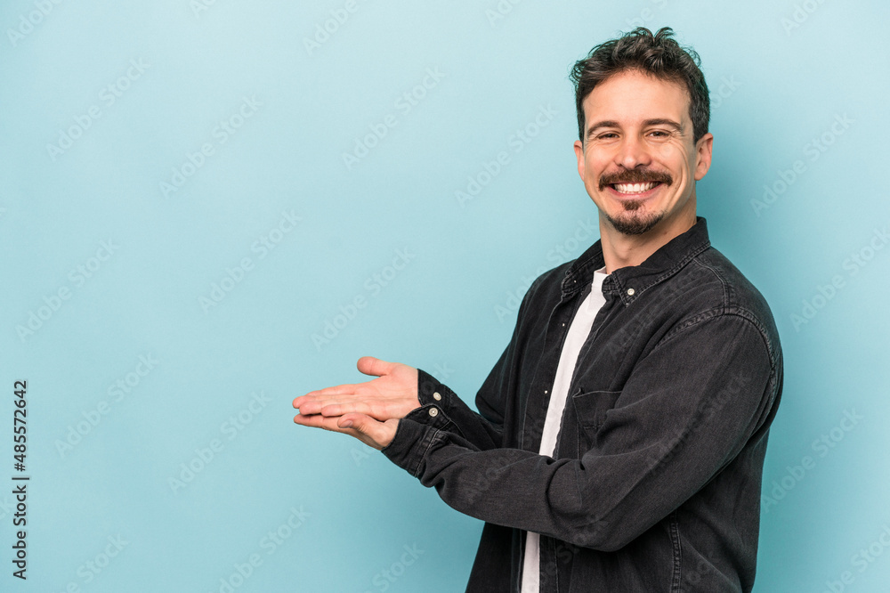 Young caucasian man isolated on blue background holding a copy space on a palm. Young caucasian man isolated on blue background holding a copy space on a palm.