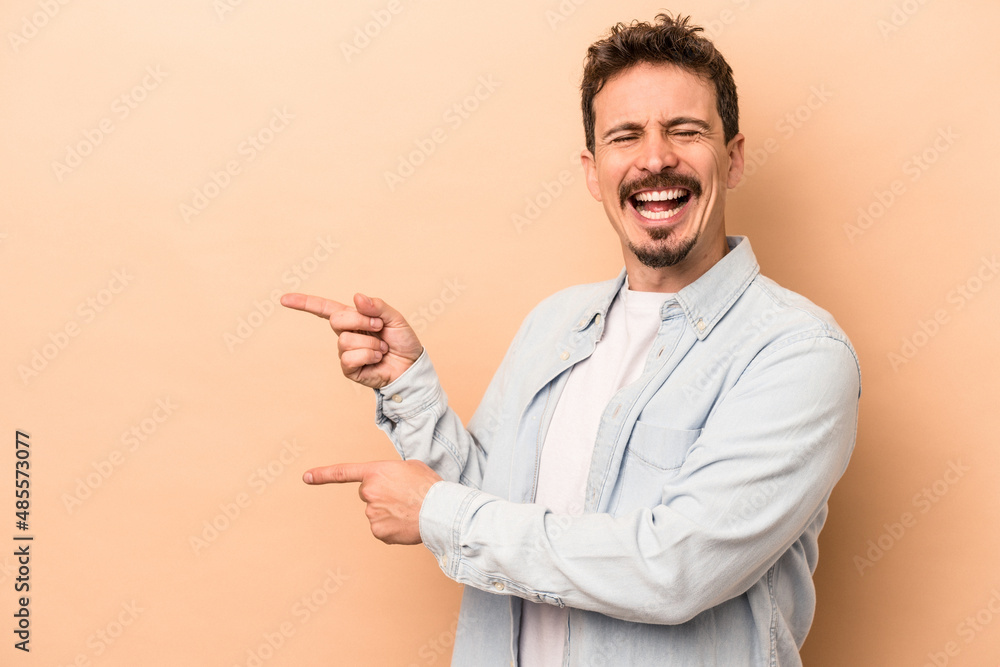 Young caucasian man isolated on beige background pointing with forefingers to a copy space, expressing excitement and desire. Young caucasian man isolated on beige background pointing with forefingers to a copy space, expressing excitement and desire.