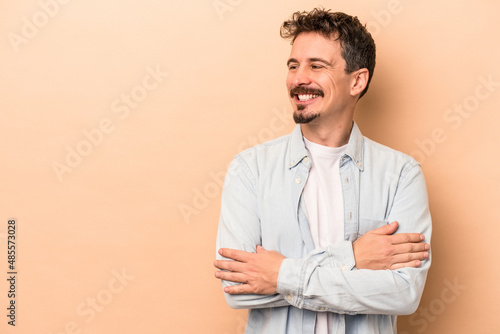 Young caucasian man isolated on beige background smiling confident with crossed arms.