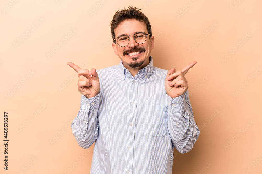 Young caucasian man isolated on beige background pointing to different copy spaces, choosing one of them, showing with finger. Young caucasian man isolated on beige background pointing to different copy spaces, choosing one of them, showing with finger.