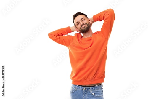 a bearded middle-aged man in orange clothes stretches with his hands folded behind his head