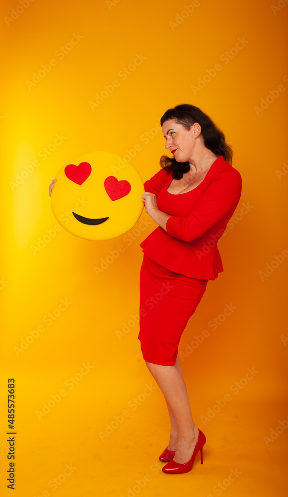 A woman in red dress shoes holds a smiley heart in her hands on a yellow background on March 8, February 14 Valentine's Day A woman in red dress shoes holds a smiley heart in her hands on a yellow background on March 8, February 14 Valentine's Day