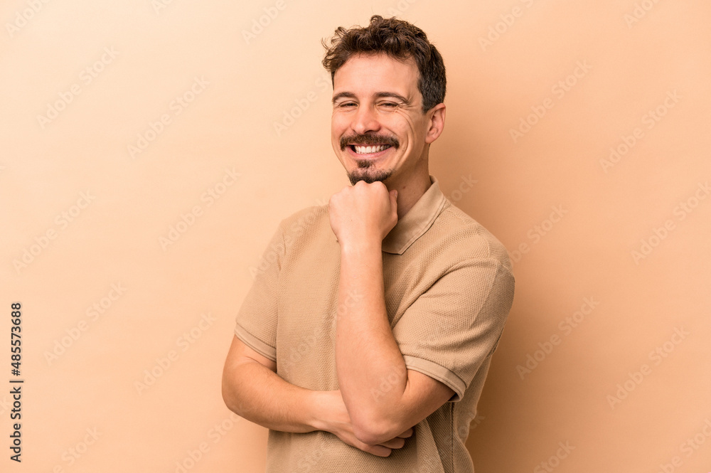 Young caucasian man isolated on beige background smiling happy and confident, touching chin with hand. Young caucasian man isolated on beige background smiling happy and confident, touching chin with hand.