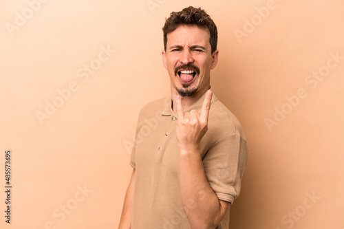 фотографія Young caucasian man isolated on beige background showing rock gesture with finge