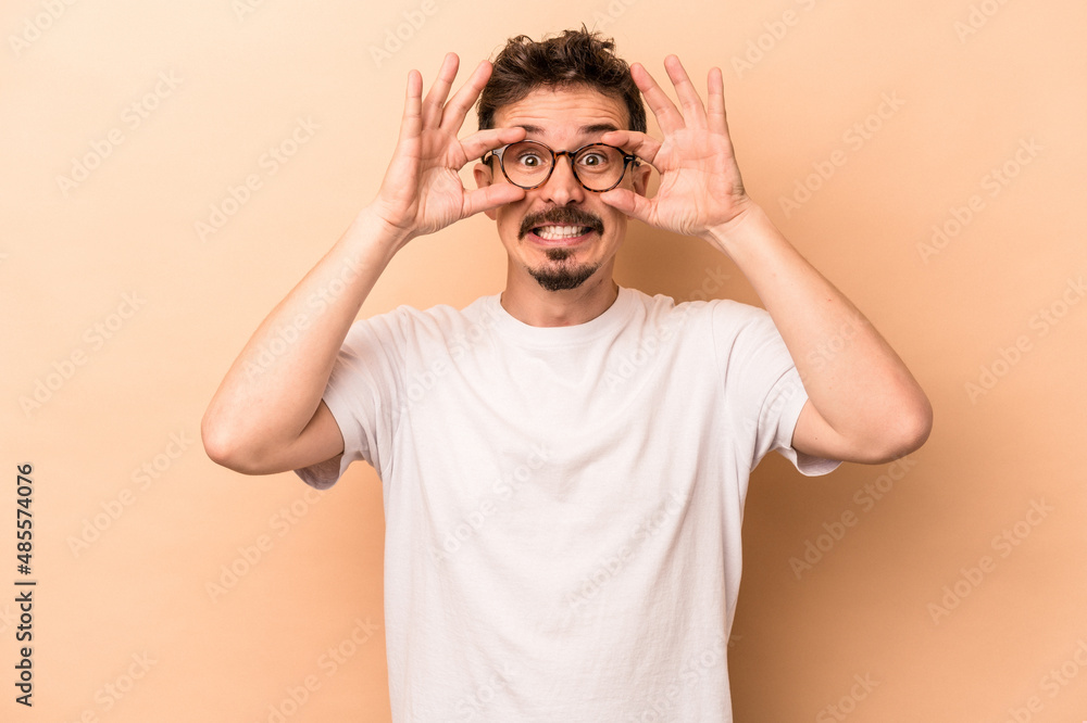 Young caucasian man isolated on beige background keeping eyes opened to find a success opportunity. Young caucasian man isolated on beige background keeping eyes opened to find a success opportunity.