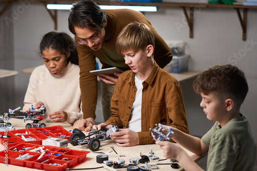 Portrait of blonde young boy building robot with diverse group of children in engineering class at modern school