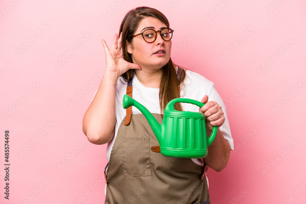 Young gardener caucasian overweight woman holding watering can isolated background trying to listening a gossip.