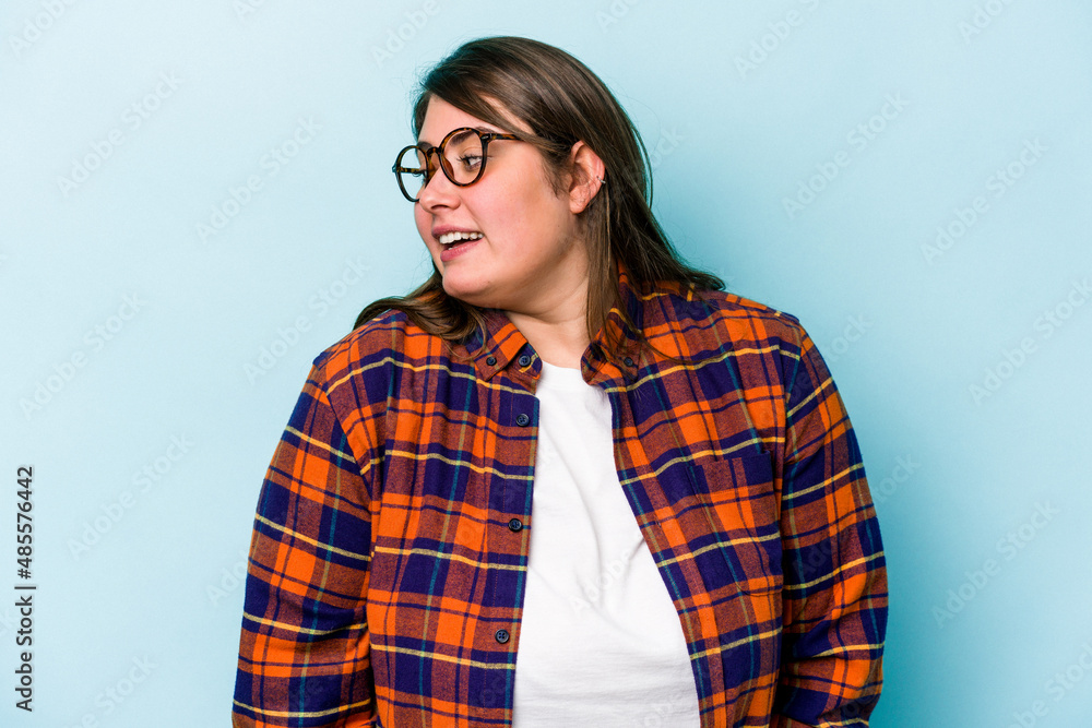 Young caucasian overweight woman isolated on blue background looks aside smiling, cheerful and pleasant. Young caucasian overweight woman isolated on blue background looks aside smiling, cheerful and pleasant.
