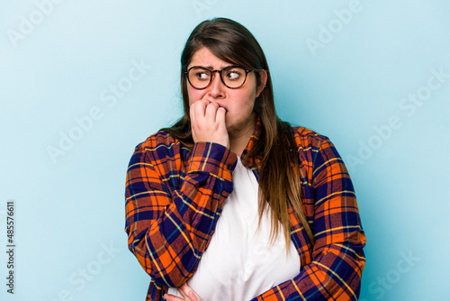 Young caucasian overweight woman isolated on blue background biting fingernails, nervous and very anxious.