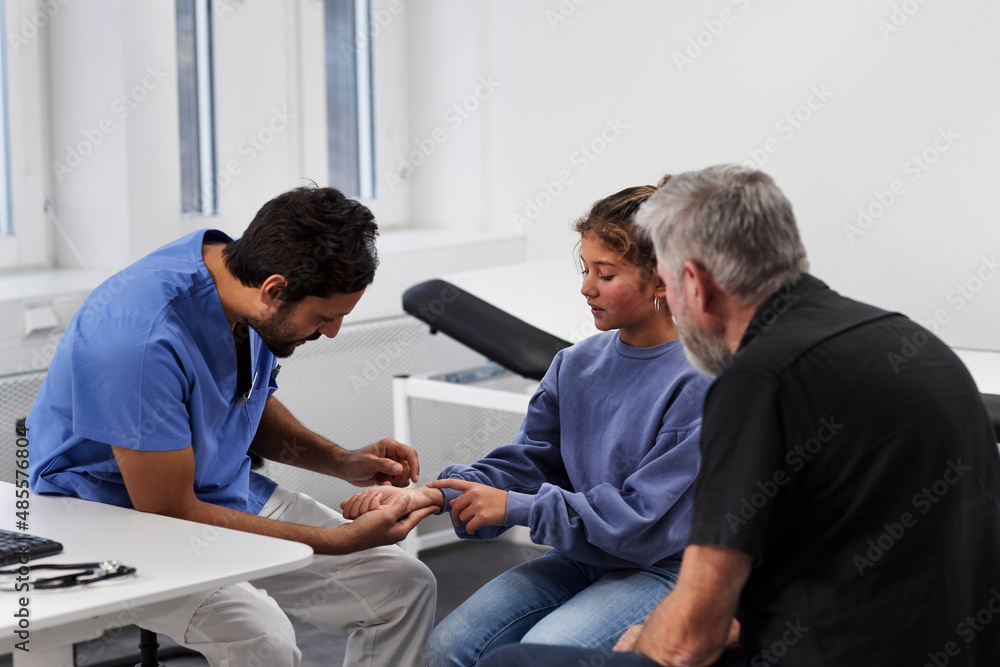 Male doctor examining girl patient's wrist during appointment Male doctor examining girl patient's wrist during appointment