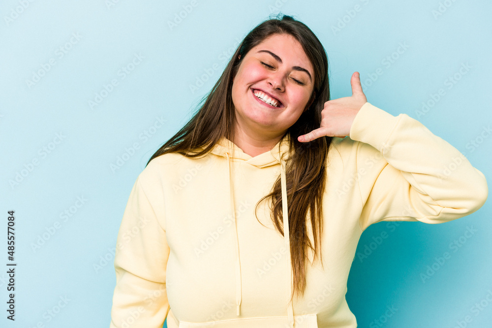 Fototapeta premium Young caucasian overweight woman isolated on blue background showing a mobile phone call gesture with fingers.