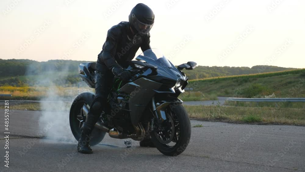 Biker performing tire burnout with lots of smoke. Motorcycle wheel are slip on route during start of movement. Wheel of sport motorbike starting to spin at asphalt road. Slow motion Close up Side view Biker performing tire burnout with lots of smoke. Motorcycle wheel are slip on route during start of movement. Wheel of sport motorbike starting to spin at asphalt road. Slow motion Close up Side view