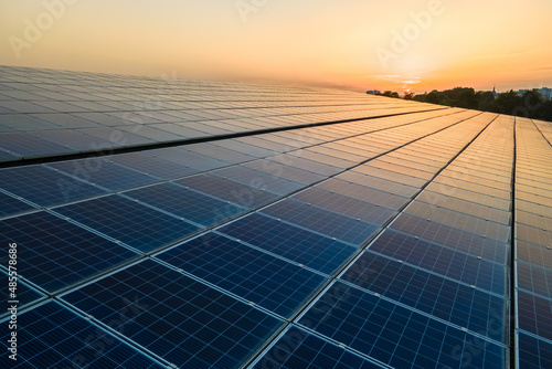 Blue photovoltaic solar panels mounted on building roof for producing clean ecological electricity at sunset. Production of renewable energy concept