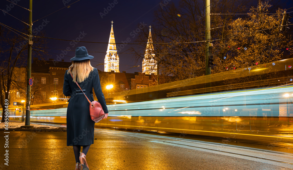 Φωτογραφία Young woman in black clothes walking on the street - Tram moving on a street at
