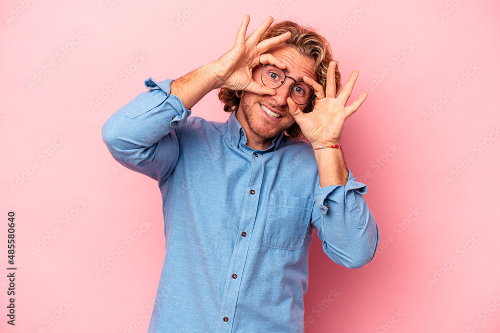 Young caucasian man isolated on pink background showing okay sign over eyes Young caucasian man isolated on pink background showing okay sign over eyes