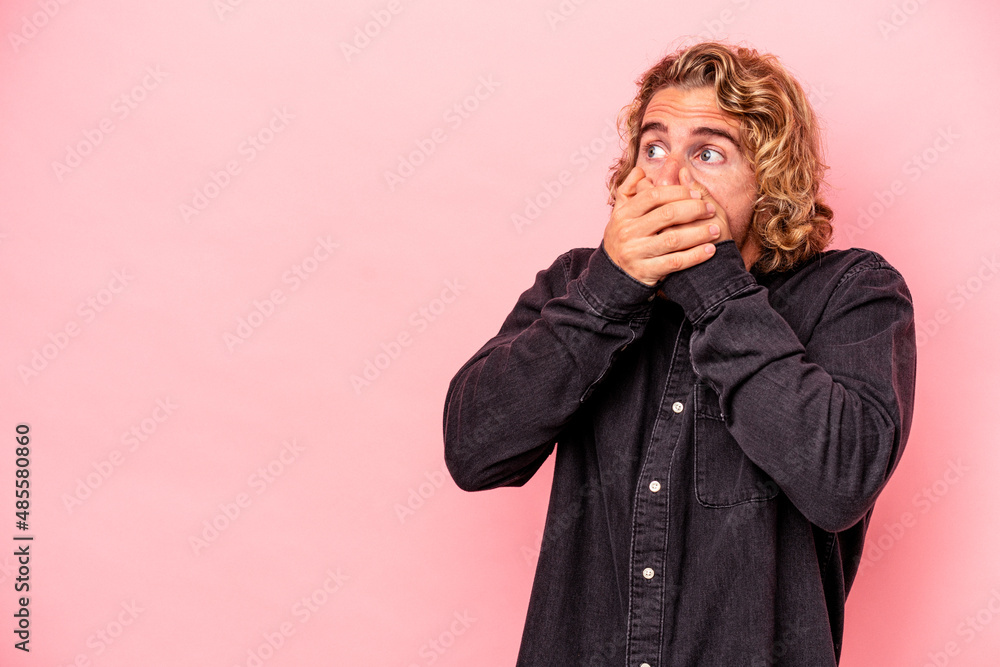 Young caucasian man isolated on pink background thoughtful looking to a copy space covering mouth with hand. Young caucasian man isolated on pink background thoughtful looking to a copy space covering mouth with hand.