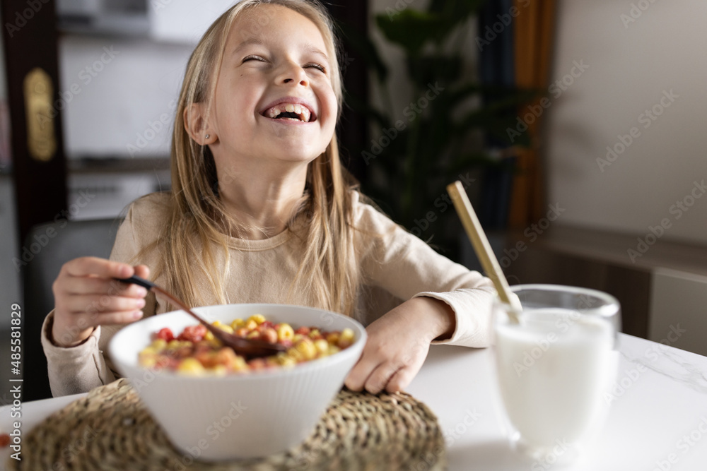 Cute little caucasian girl sitting at table on kitchen early morning and preparing breakfast with colorful cornflakes and milk. Kid enjoying life with healthful food, healthy lifestyle concept Cute little caucasian girl sitting at table on kitchen early morning and preparing breakfast with colorful cornflakes and milk. Kid enjoying life with healthful food, healthy lifestyle concept