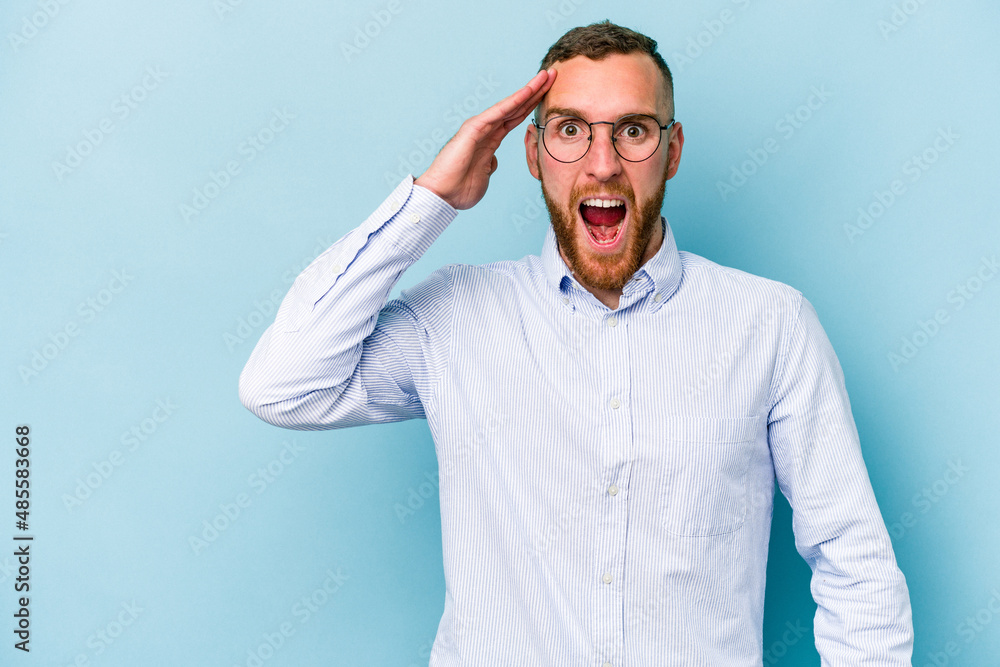Young caucasian man isolated on blue background shouts loud, keeps eyes opened and hands tense. Young caucasian man isolated on blue background shouts loud, keeps eyes opened and hands tense.