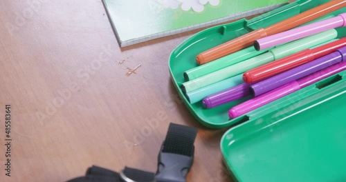 Welsh corgi pembroke white paw picks up black felt-tip pen from pile of school supplies on wooden desk IN classroom closeup photo