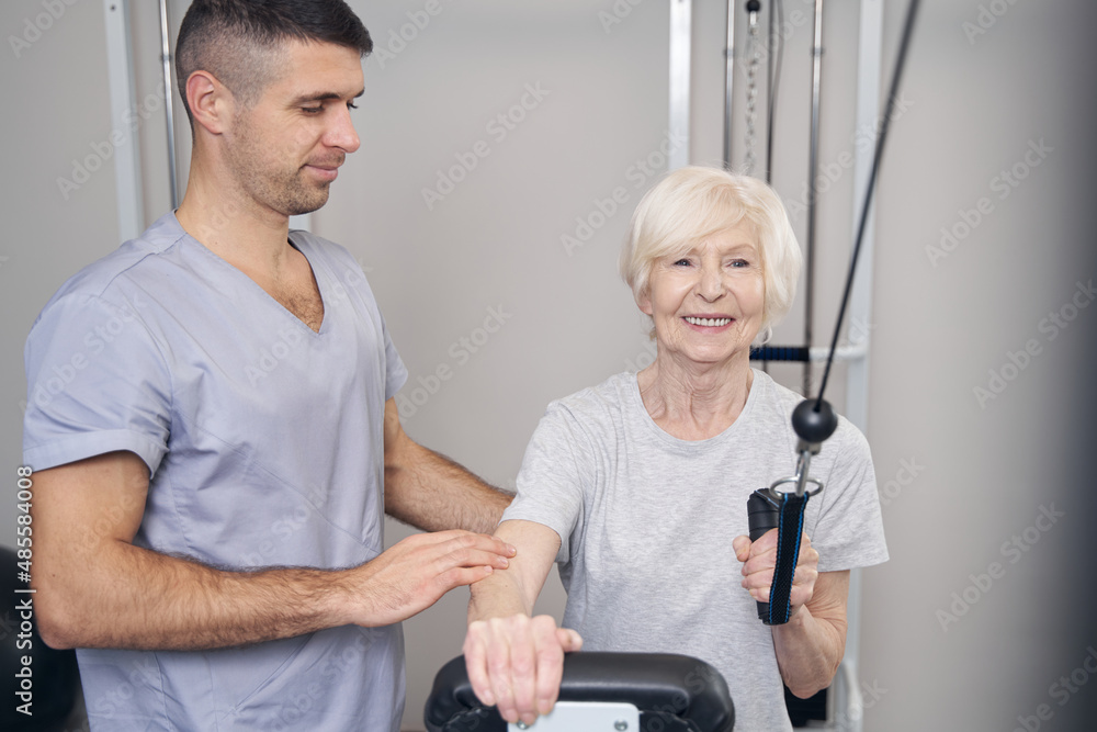 Obraz premium Aged female holding board while pulling cable of gym machine