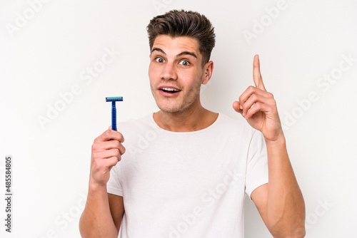 Young caucasian man shaving his beard isolated on white background having an idea, inspiration concept.