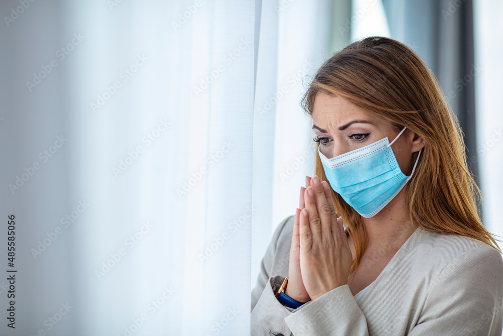 Hopeful female employee in protective face mask praying in office for coronavirus be finished, woman believer feel superstitious religious during covid-19 pandemic at workplace.