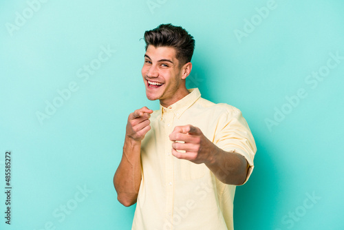 Young caucasian man isolated on blue background cheerful smiles pointing to front.