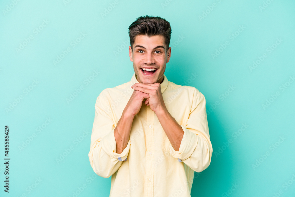 Young caucasian man isolated on blue background praying for luck, amazed and opening mouth looking to front.