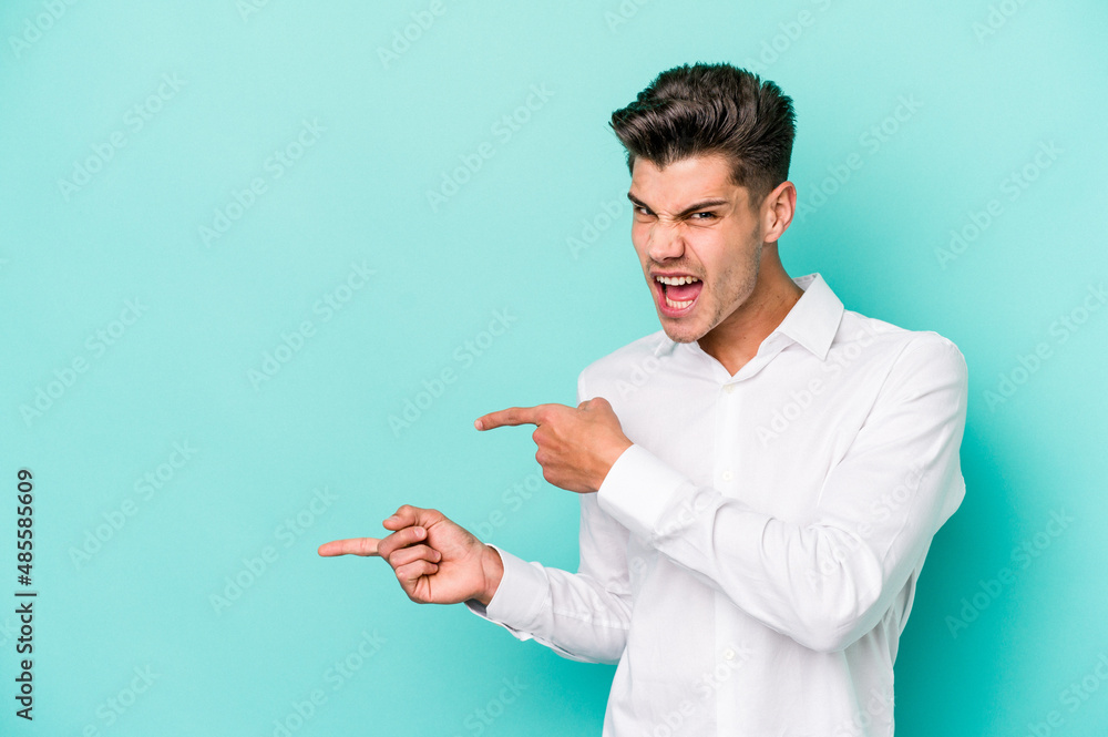 Young caucasian man isolated on blue background pointing with forefingers to a copy space, expressing excitement and desire. Young caucasian man isolated on blue background pointing with forefingers to a copy space, expressing excitement and desire.