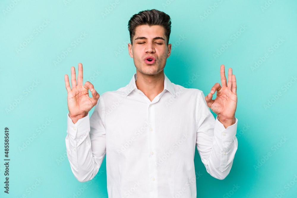 Young caucasian man isolated on blue background relaxes after hard working day, she is performing yoga. Young caucasian man isolated on blue background relaxes after hard working day, she is performing yoga.