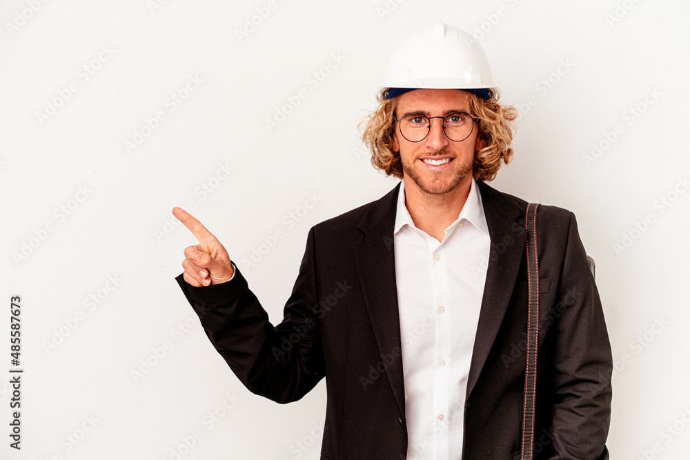Young architect caucasian man with helmet isolated on white background smiling and pointing aside, showing something at blank space.