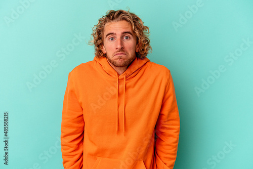 Foto Young caucasian man isolated on blue background shrugs shoulders and open eyes confused