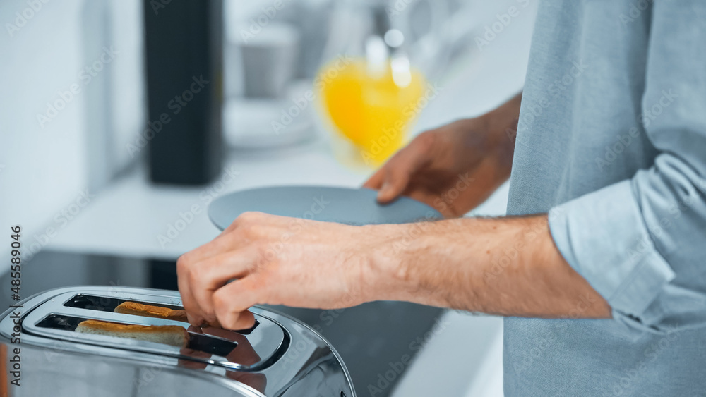 cropped view of man preparing toasts in electric toaster in kitchen
