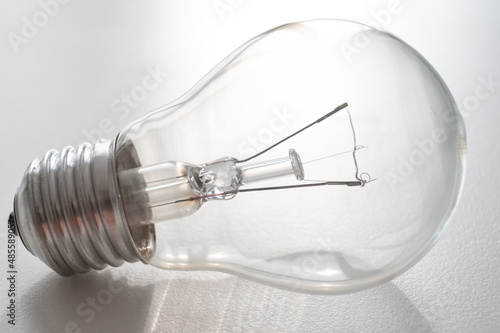 Incandescent light bulb, on a white surface, photographed against the light. Cost of electricity and lighting. Lighting devices.
