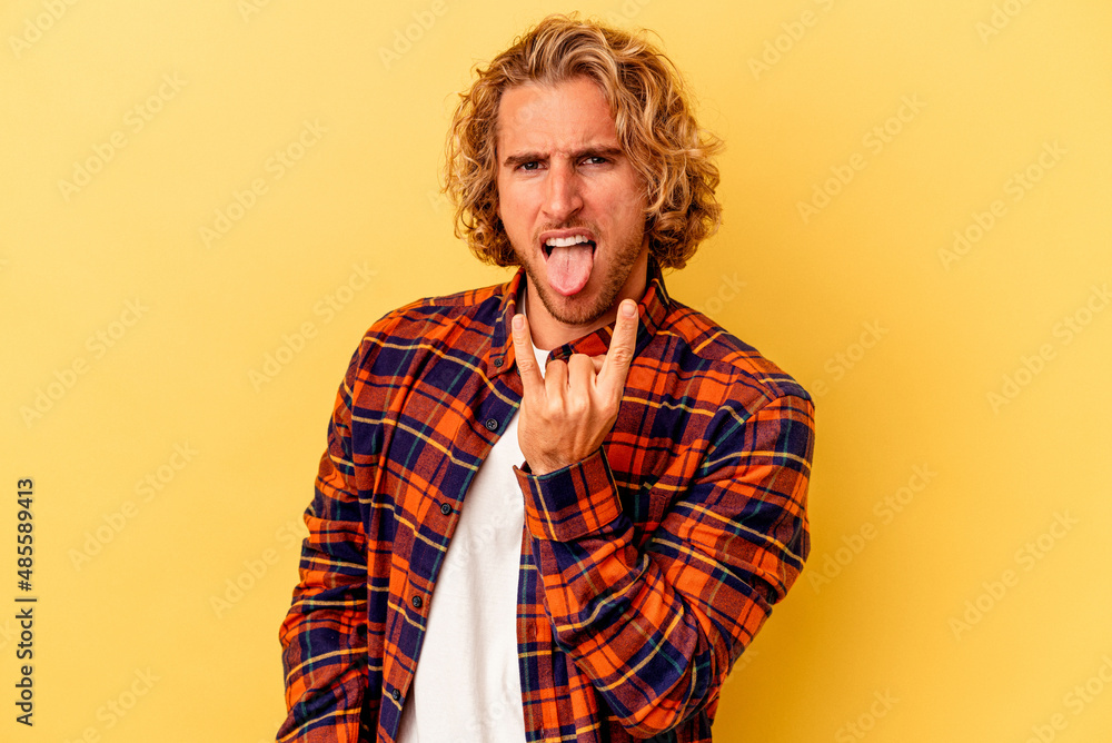 Young caucasian man isolated on yellow background showing rock gesture with fingers Young caucasian man isolated on yellow background showing rock gesture with fingers
